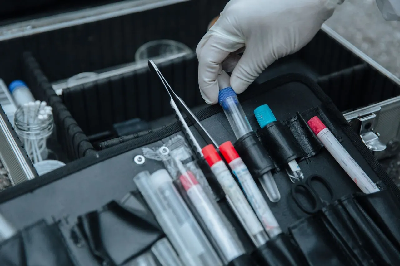 A gloved hand lifts a swab with tweezers from a forensic collection kit of labeled sample tubes, the laboratory training behind affordable online master's degrees in forensic science for California students