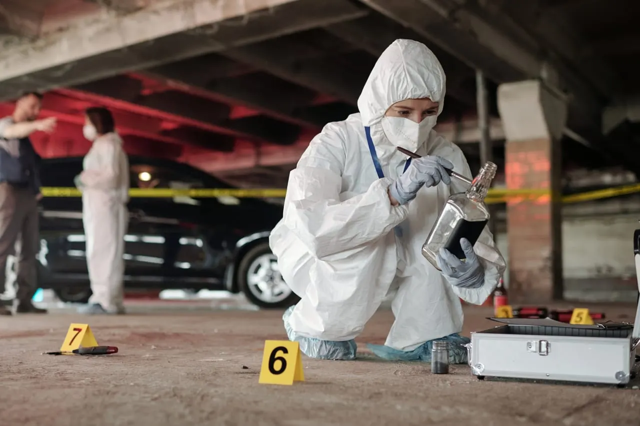 A forensic investigator in protective coveralls examines evidence at a marked scene while colleagues confer nearby, the field work behind CSI and forensic science degrees in California