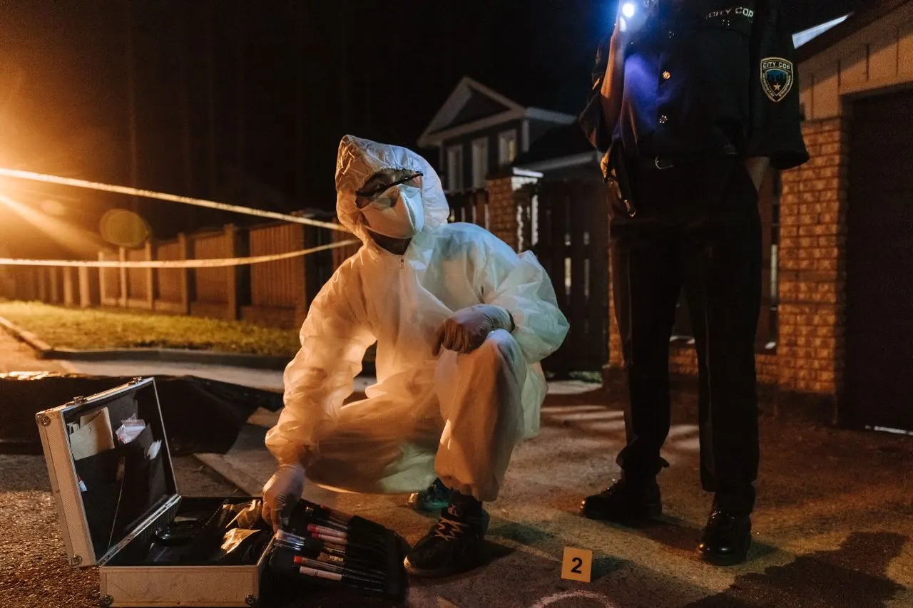 A forensic technician works an open evidence kit at a taped-off night scene as an officer lights the ground, the advanced casework California master's degrees in forensic science build toward