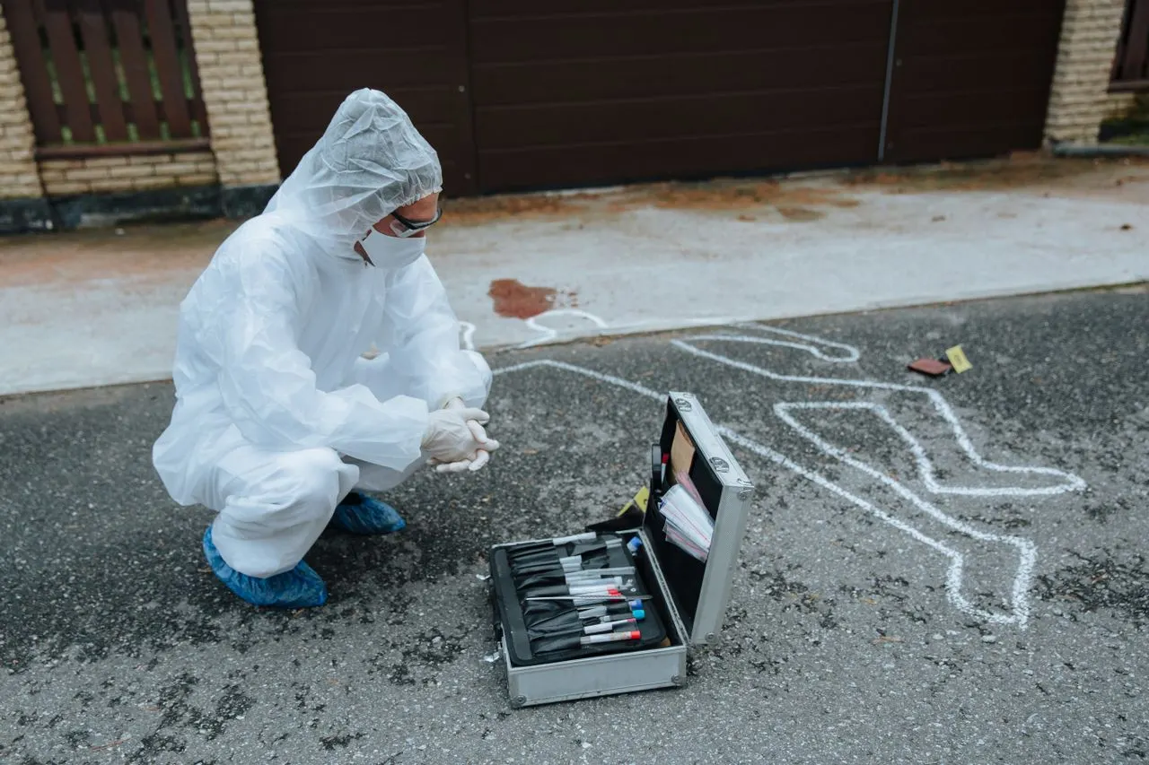 A forensic investigator in a protective suit and shoe covers works an evidence kit of labeled tubes beside a chalk outline, the casework behind online master's degrees in forensic science for California students