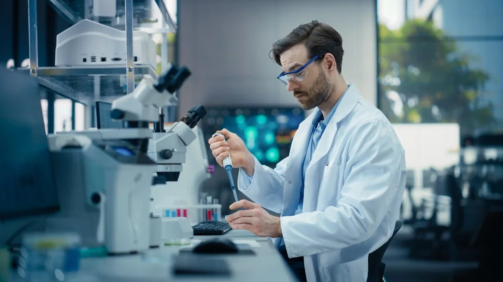 Scientist using a pipette beside a microscope in a laboratory