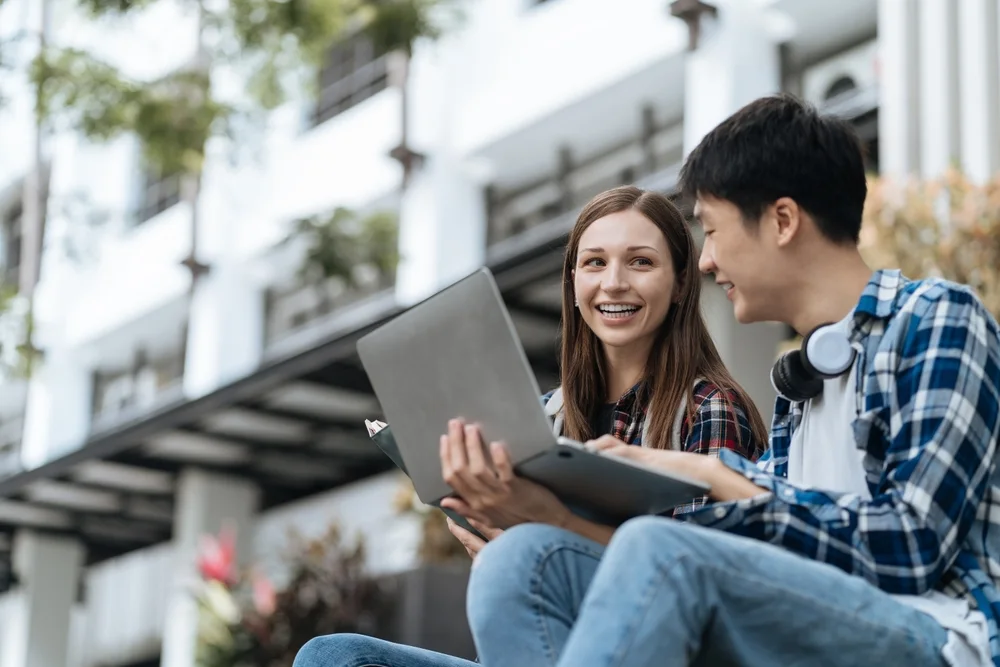 Two students with a laptop on campus steps
