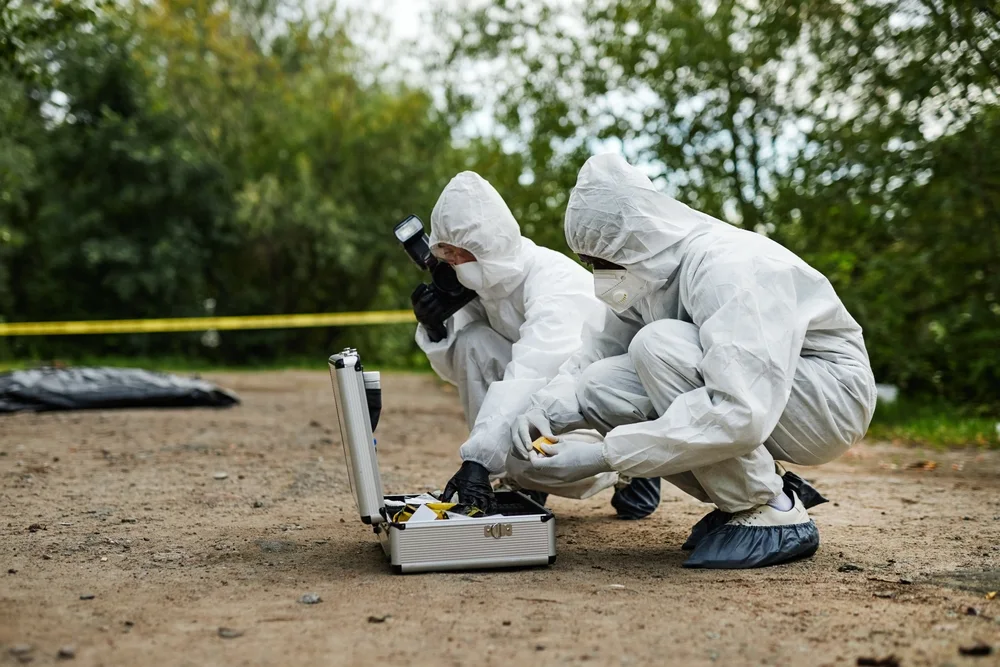 Two investigators in protective suits collecting evidence at an outdoor scene