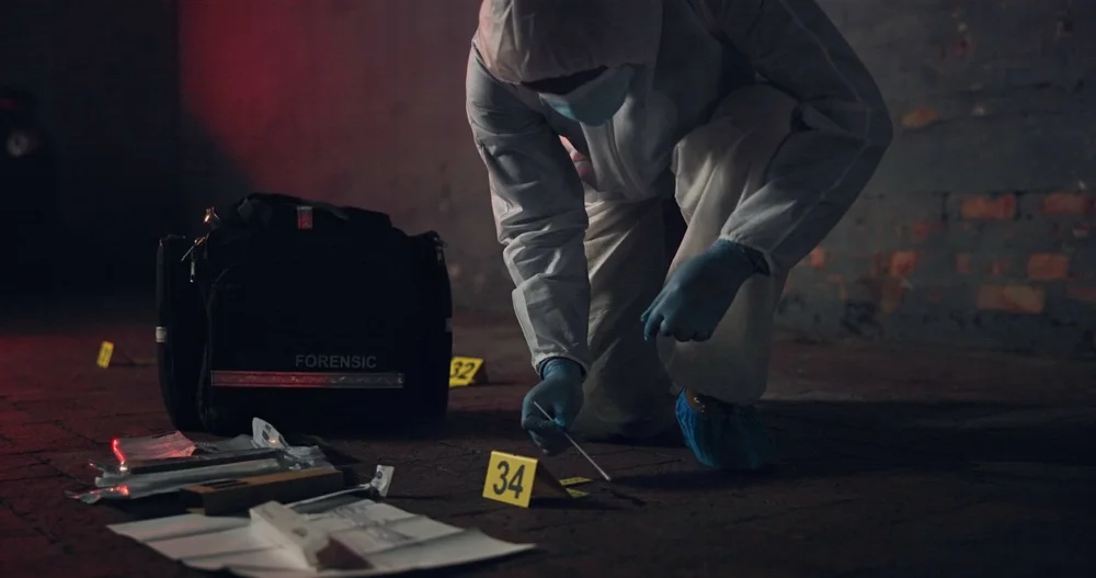 Investigator kneeling beside a forensic case and a numbered marker at night
