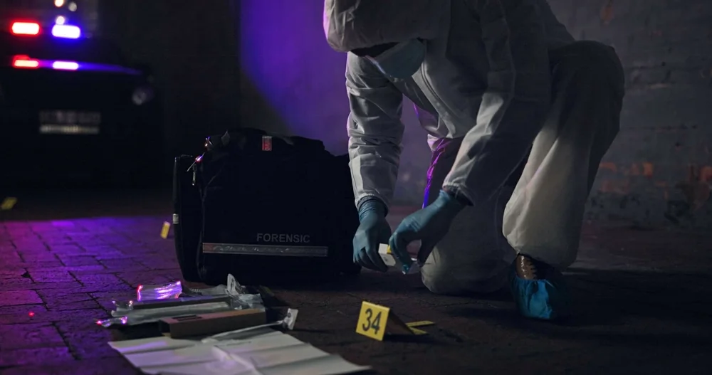 Investigator collecting evidence on a street lit by police lights