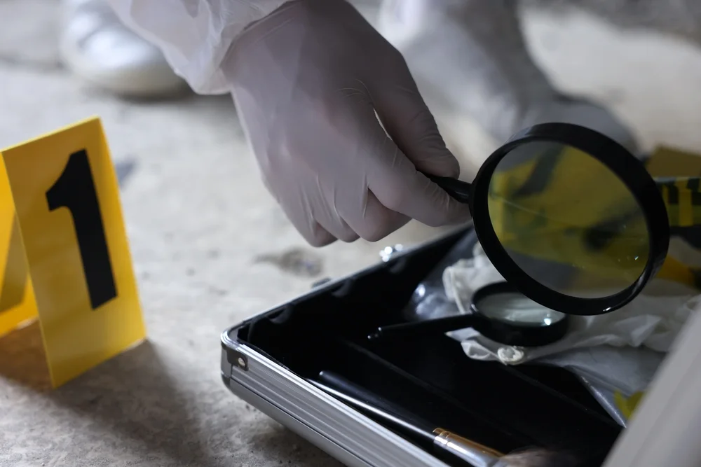 Gloved investigator examining an item with a magnifying glass beside an evidence case