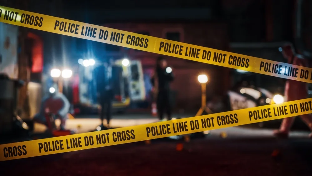 Police line tape stretched across a street with officers working behind it