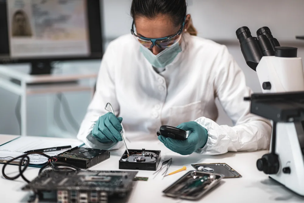 Analyst examining a disassembled hard drive beside a microscope