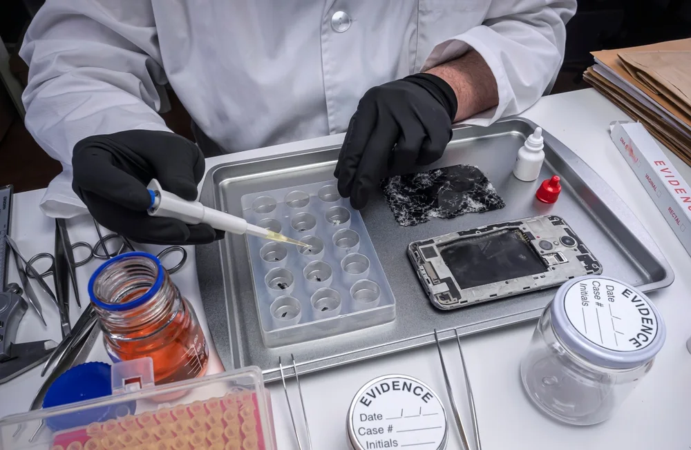 Technician sampling beside a disassembled smartphone and evidence containers