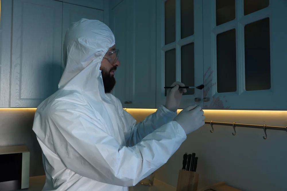 Investigator in a protective suit dusting a surface for fingerprints