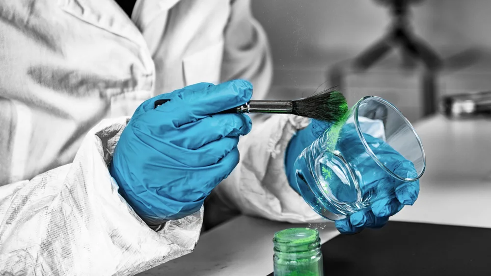 Gloved technician brushing fingerprint powder onto a glass beaker