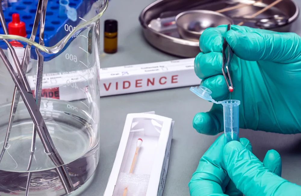 Gloved technician handling a swab tube beside evidence packaging