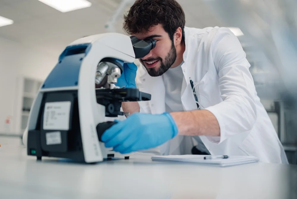 Scientist in a white coat looking through a microscope