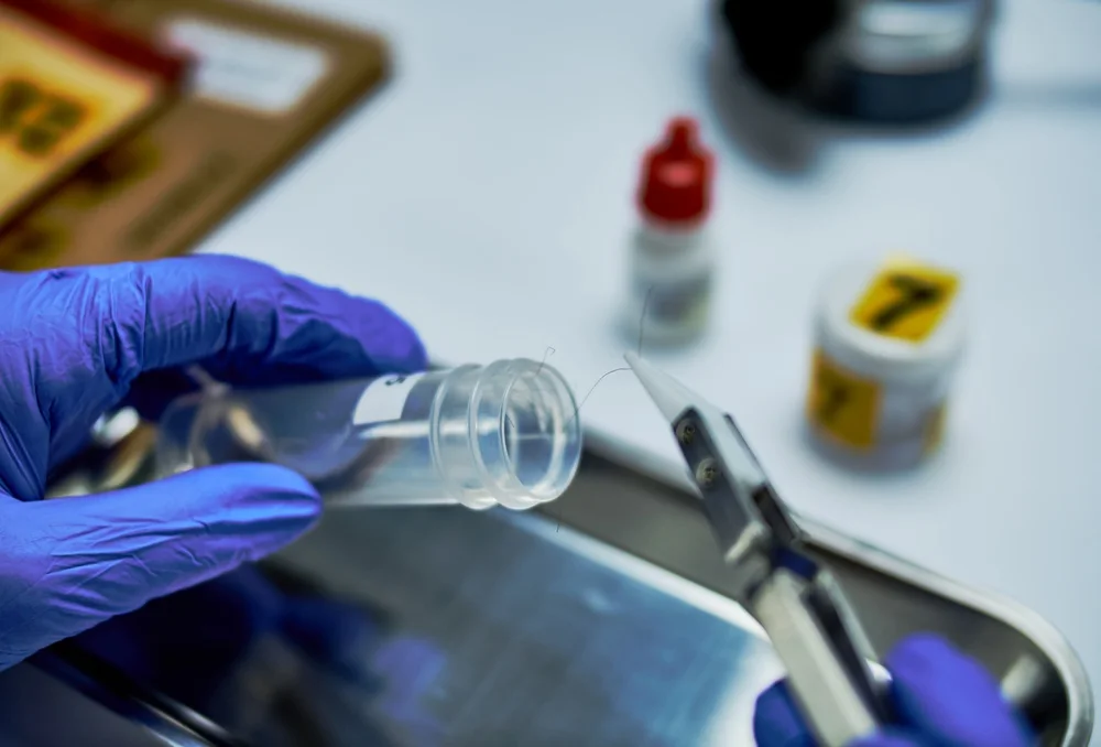 Gloved technician placing trace evidence into a tube with tweezers