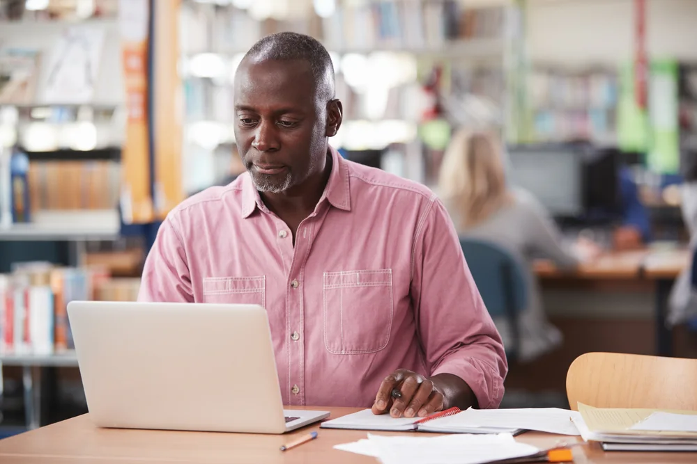Adult student working on a laptop at a library table