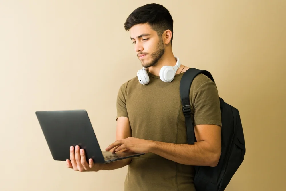 Student with a backpack holding an open laptop