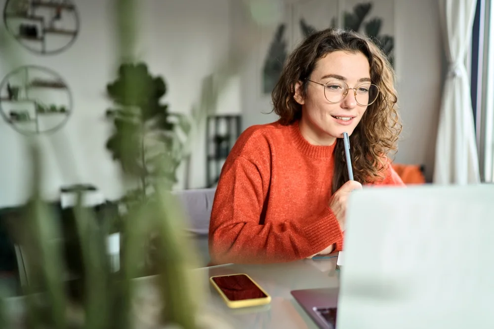 Student looking at a laptop screen while holding a pen