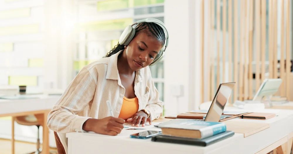 Student taking notes beside a laptop and textbooks