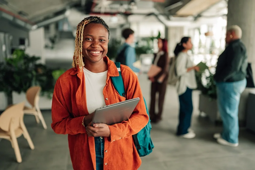 Student holding a laptop in a busy campus space